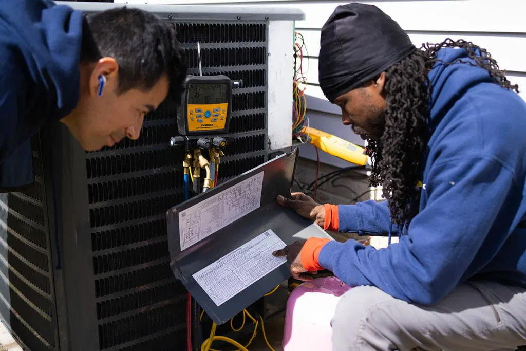 HVAC technicians inspecting outdoor air conditioning unit with refrigerant gauges service inspection