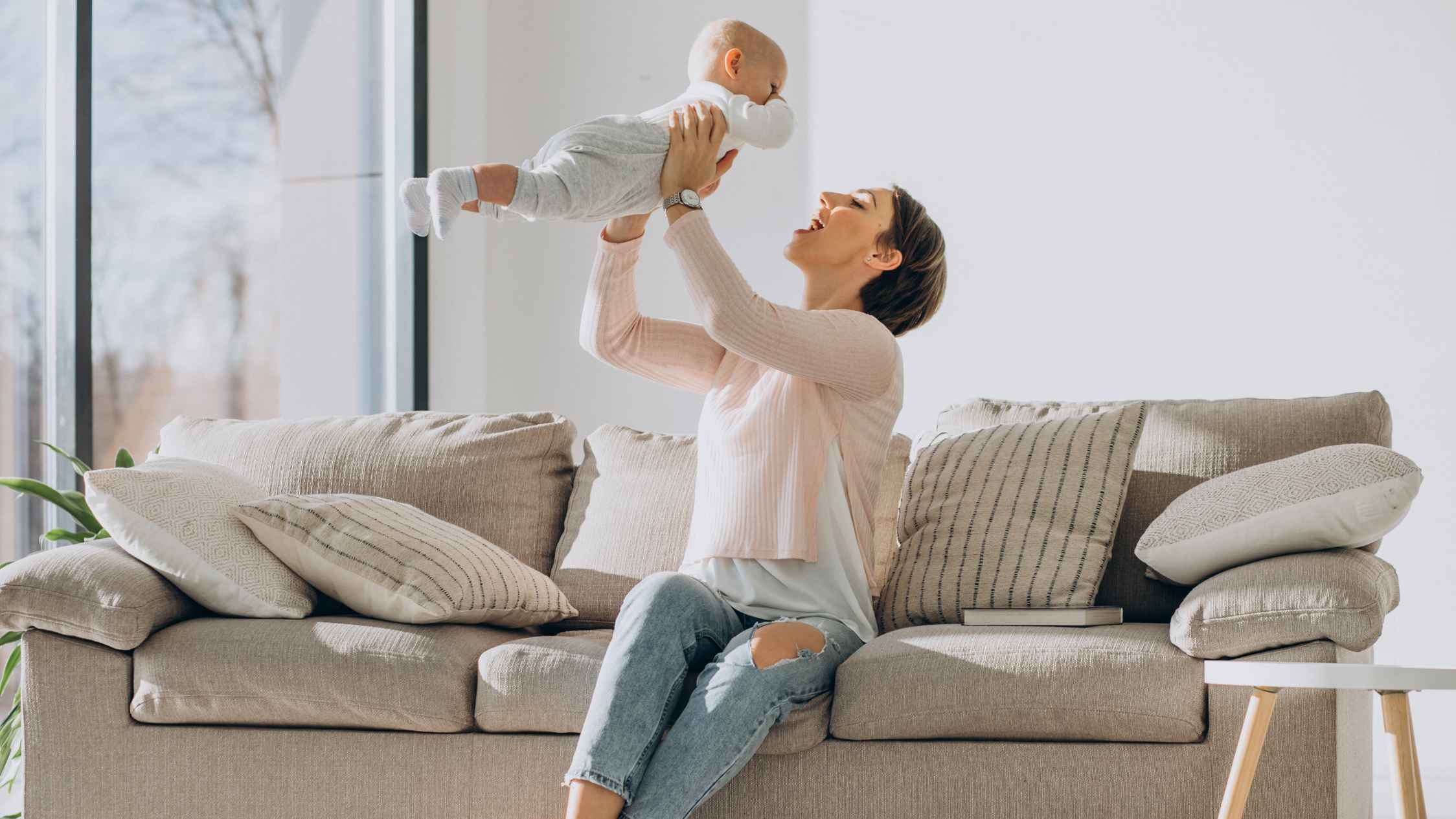 young mother and toddler son on sofa watching a robot vacuum cleaner in living room home lifestyle