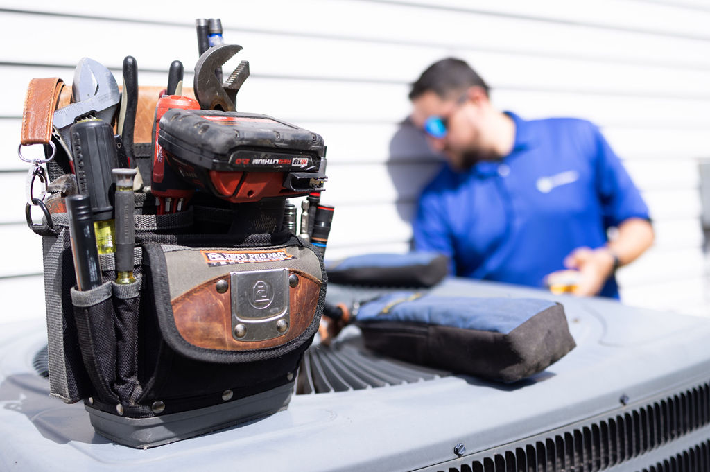 HVAC tool bag on an outdoor heating unit with a technician performing heating service in the background.