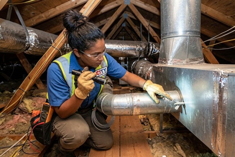 Technician adjusting HVAC dampers on attic ductwork during a home inspection to improve airflow balance and system performance